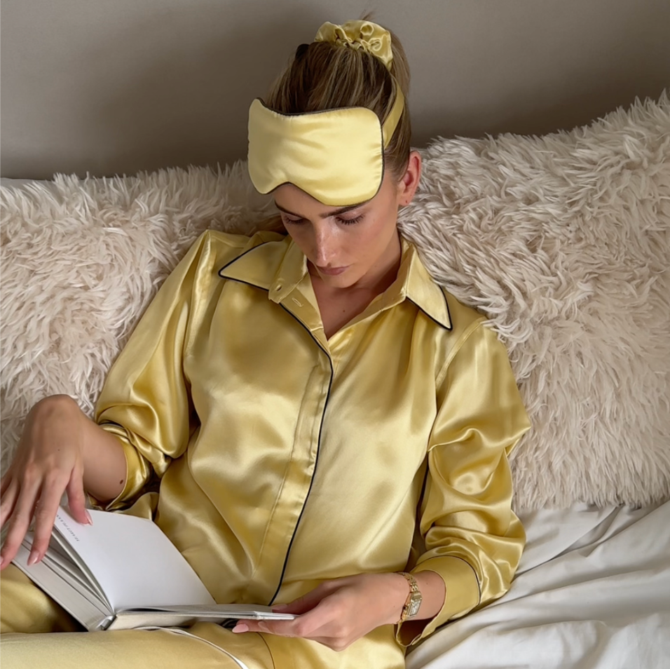 Woman in gold satin silk sleep mask and pyjamas, Nokaya, reading a book.