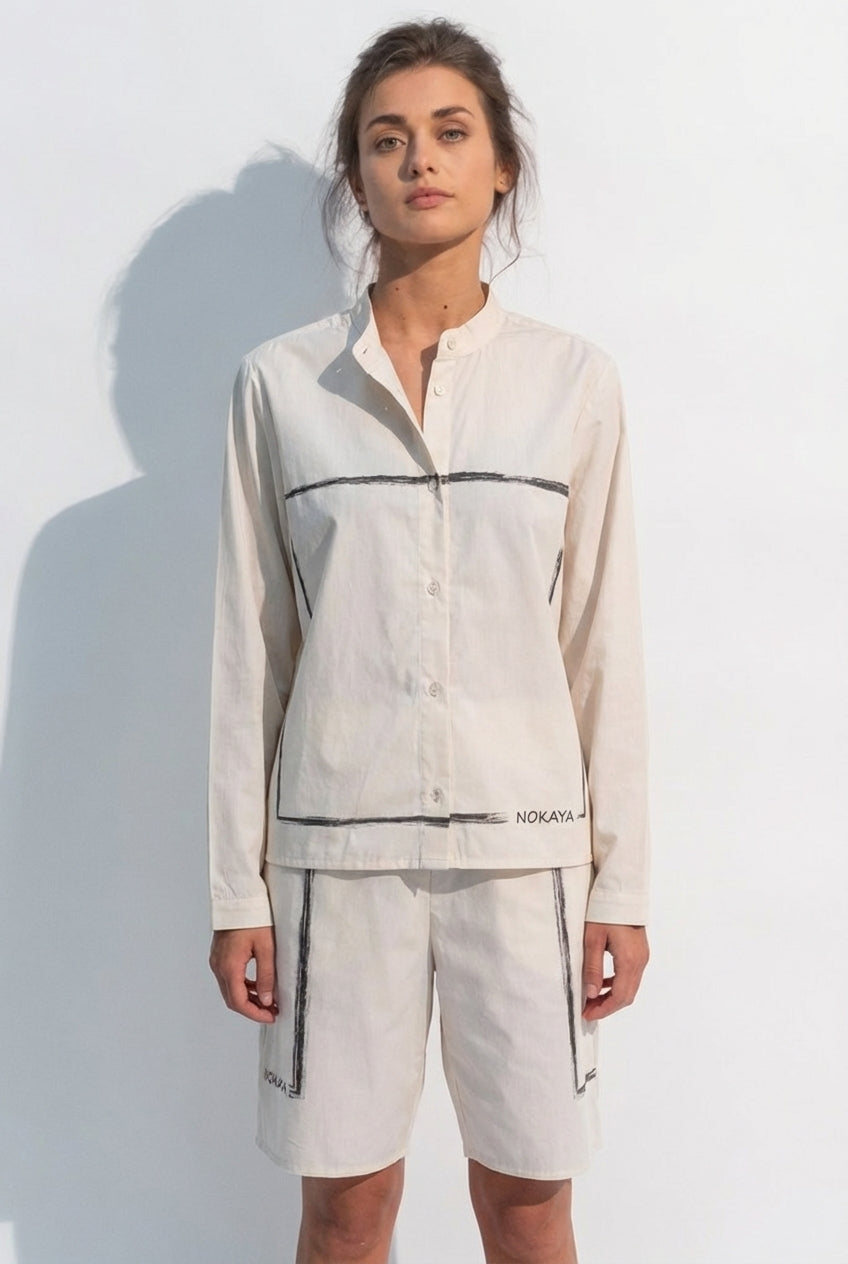 Woman wearing a light-colored cotton shirt and shorts set with black accents against a white background