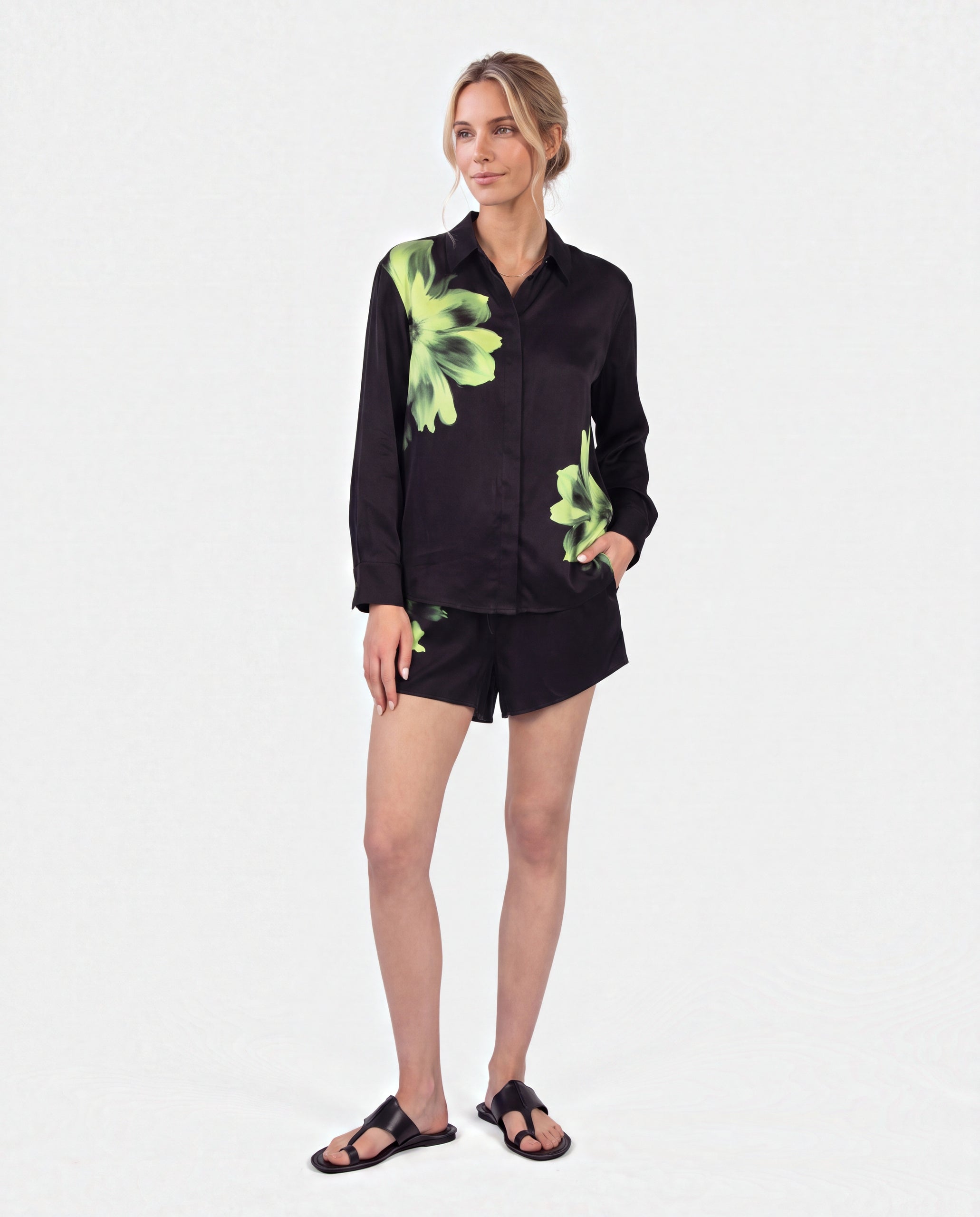 Pure-silk black long-sleeve button-up shirt and matching shorts set Nokaya with bright green floral prints, paired with black slide sandals, set against a plain white studio background.