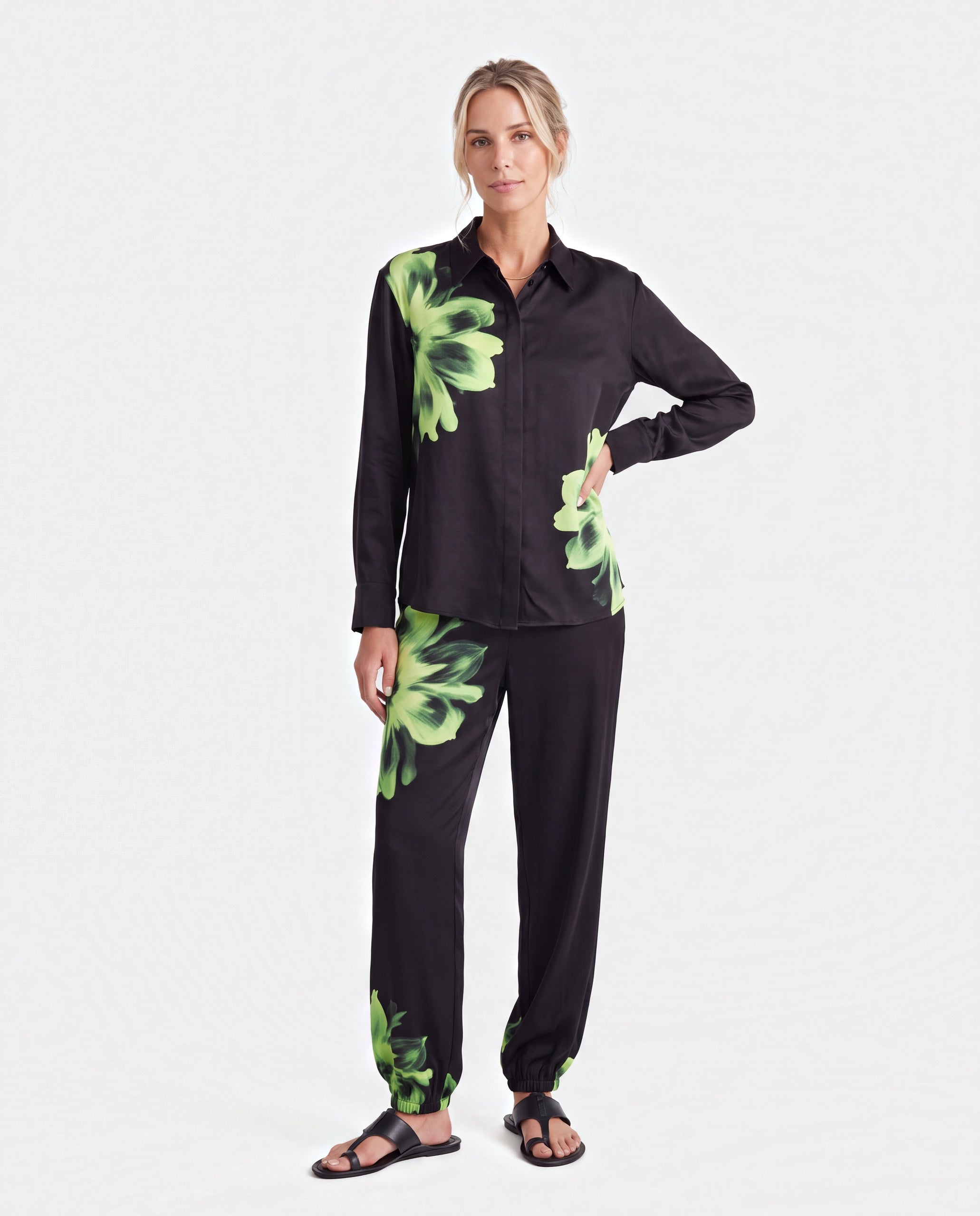 Silk matching black shirt and trousers with a vibrant green floral print, consisting of a long-sleeve button-up shirt and matching pants, against a plain light gray background. Nokaya