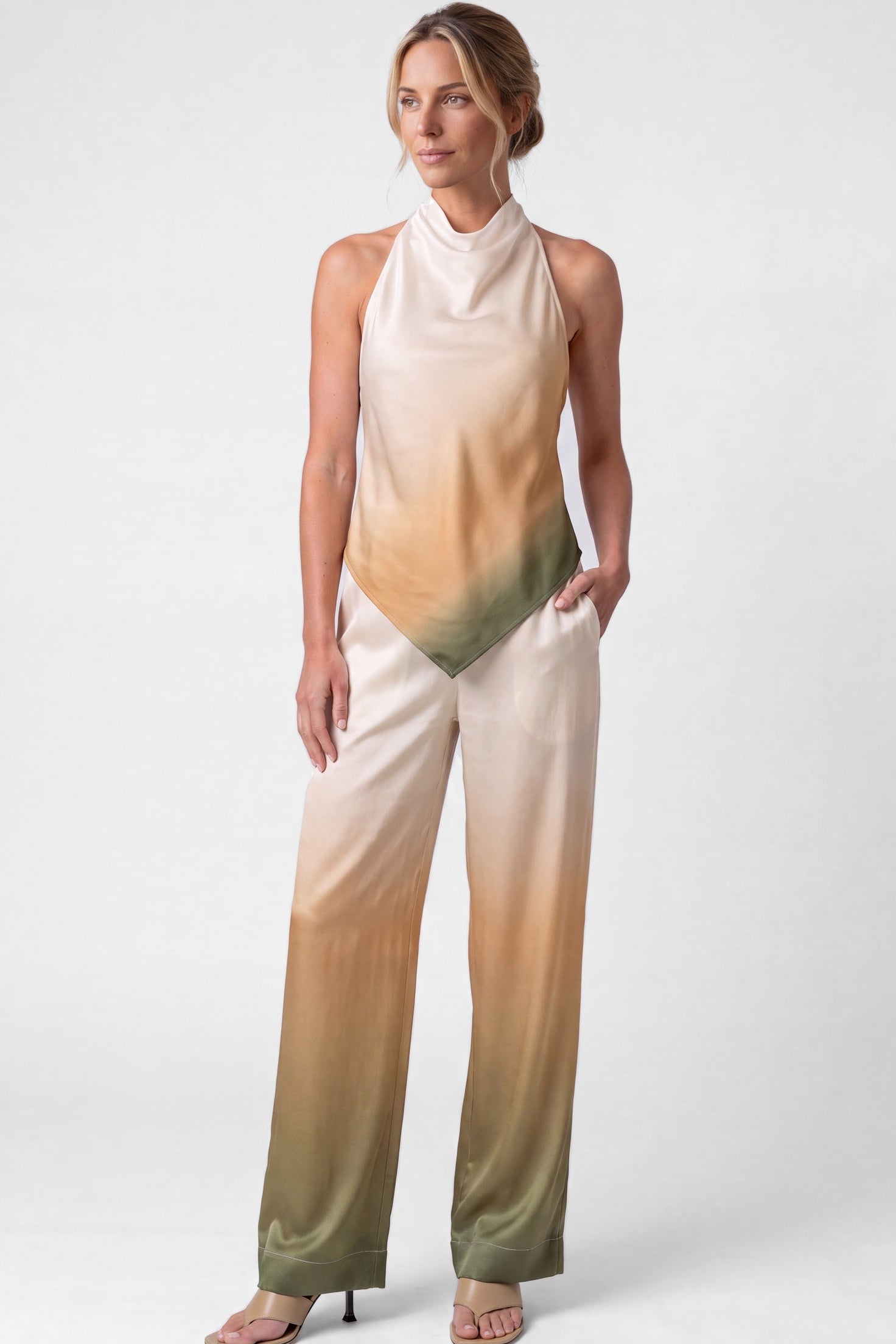 sleeveless high-neck silk top and trouses outfit Nokaya with a gradient colour-blocked design transitioning from cream to beige and olive green, paired with neutral heeled sandals against a light grey studio background.