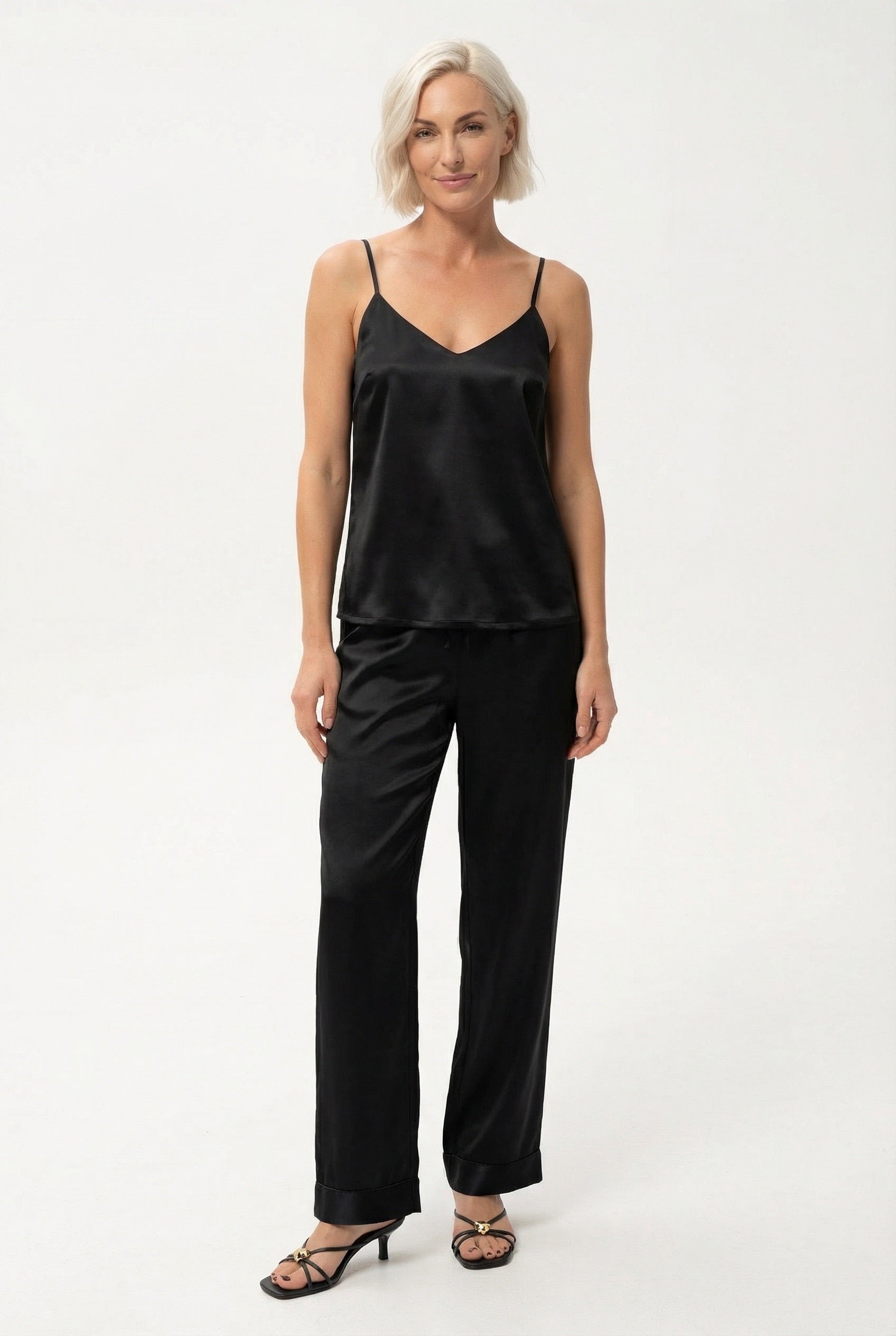 Woman wearing a black silk cami top with a V-neckline and pants Nokaya on a white background