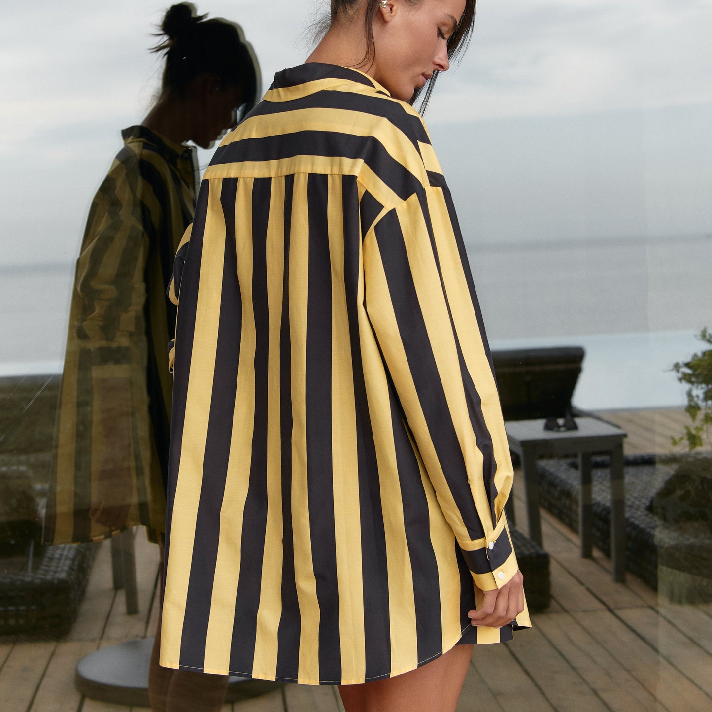 Woman wearing a black and yellow striped cotton silk dress, Nokaya, on a wooden deck. Length 80cm.