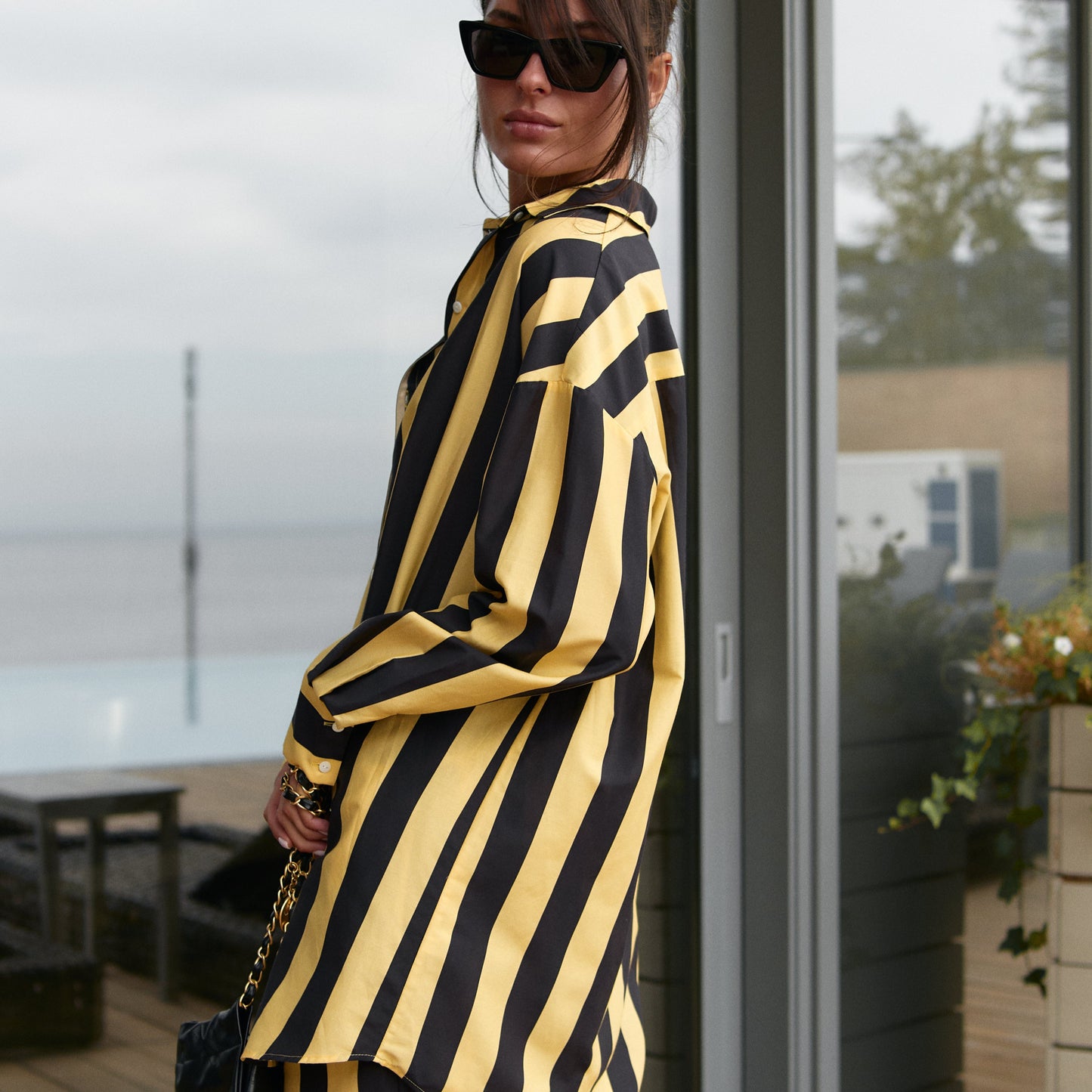 A woman wearing a black and yellow striped cotton silk shirt, Nokaya, standing in front of a glass door.
