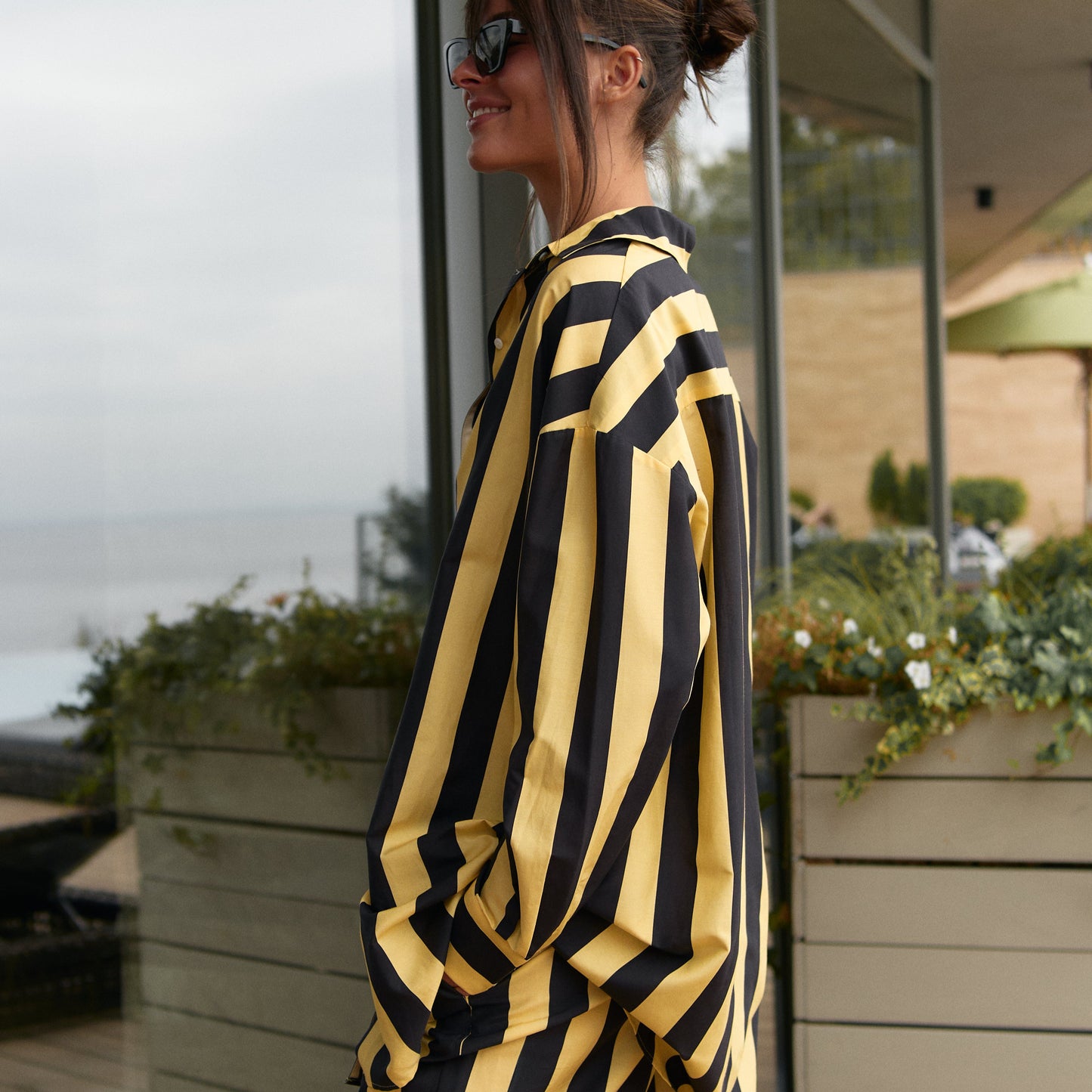 Woman in a black and yellow striped cotton silk outfit, Nokaya, standing outdoors near a modern building.