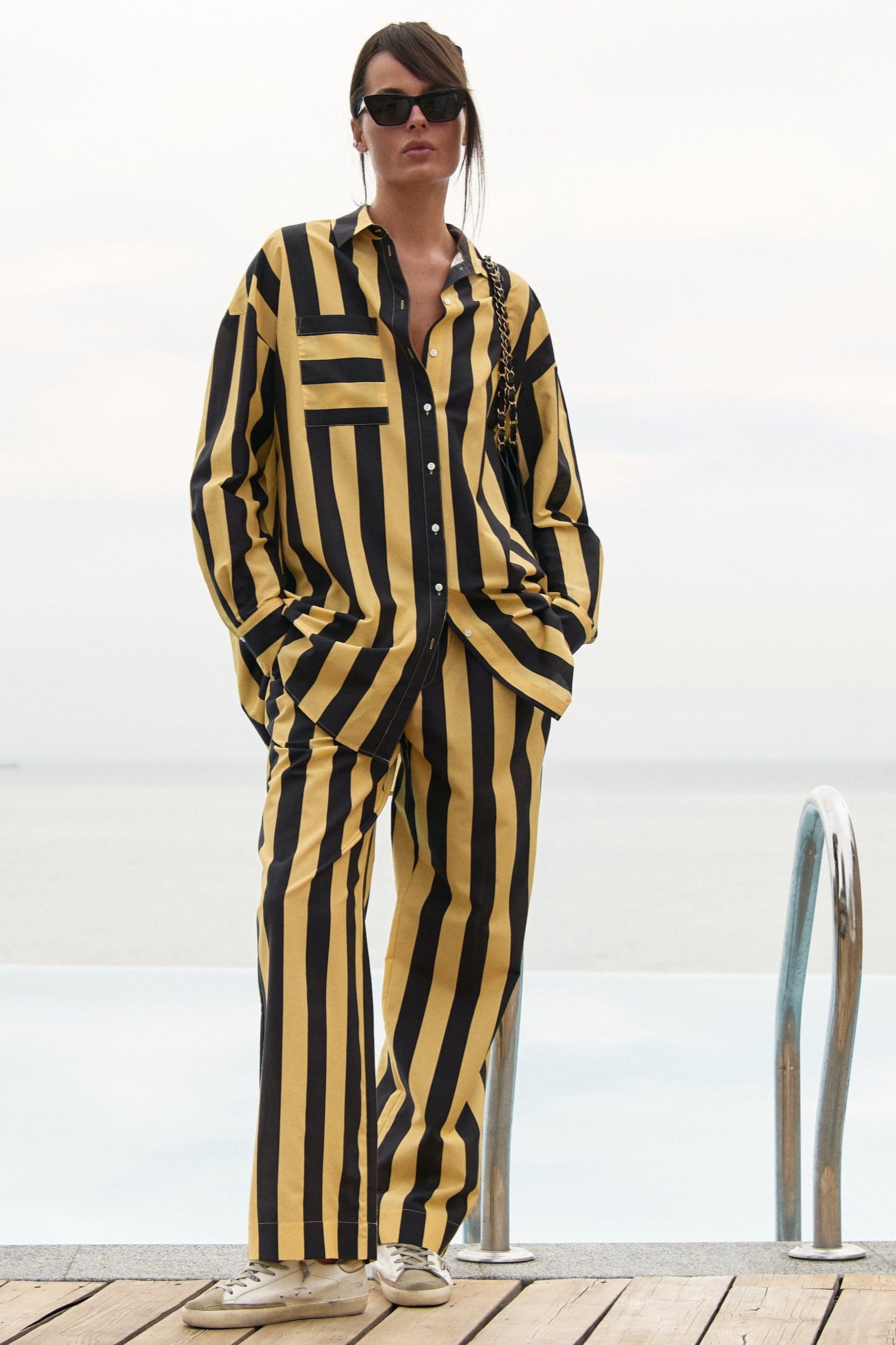 A woman wearing a black and yellow striped cotton shirt and pants, standing on a wooden deck with a white background