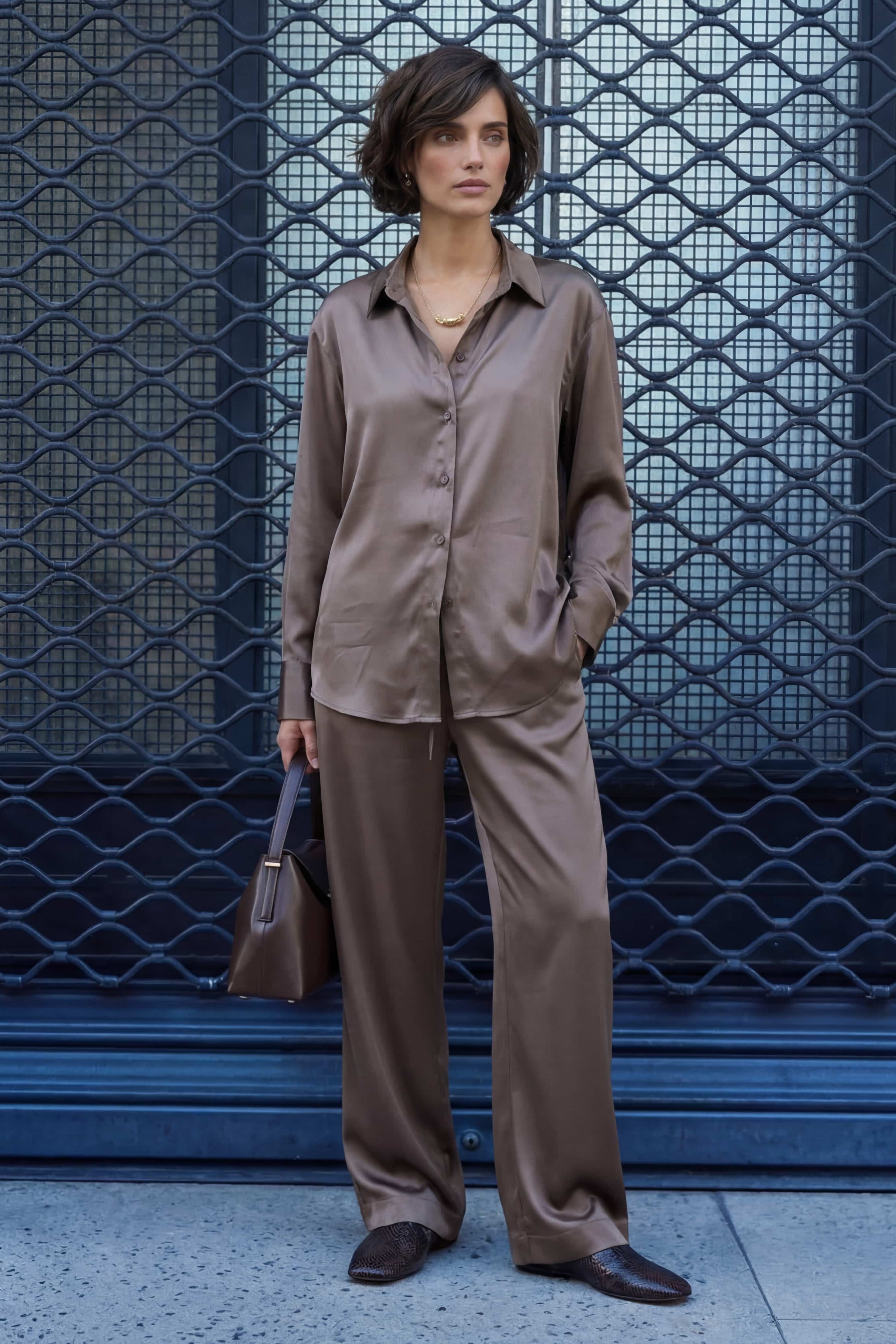 Woman in silk brown outfit Nokaya The Lady standing against a textured blue wall.