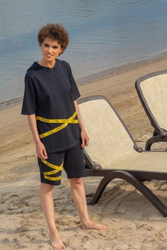 Person standing on a sandy beach with lounge chairs and water in the background