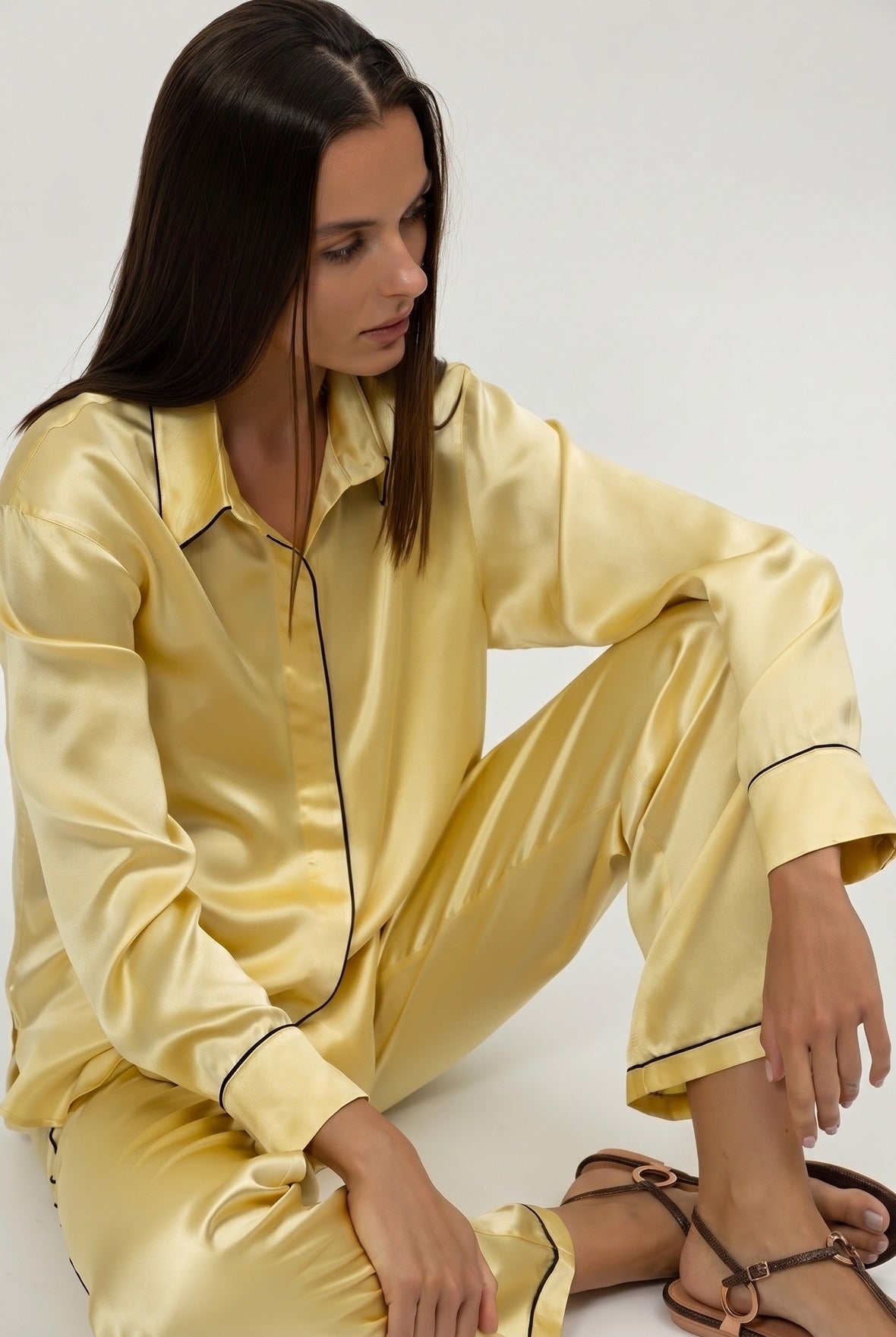A woman wearing a yellow silk satin pajama set on a plain background