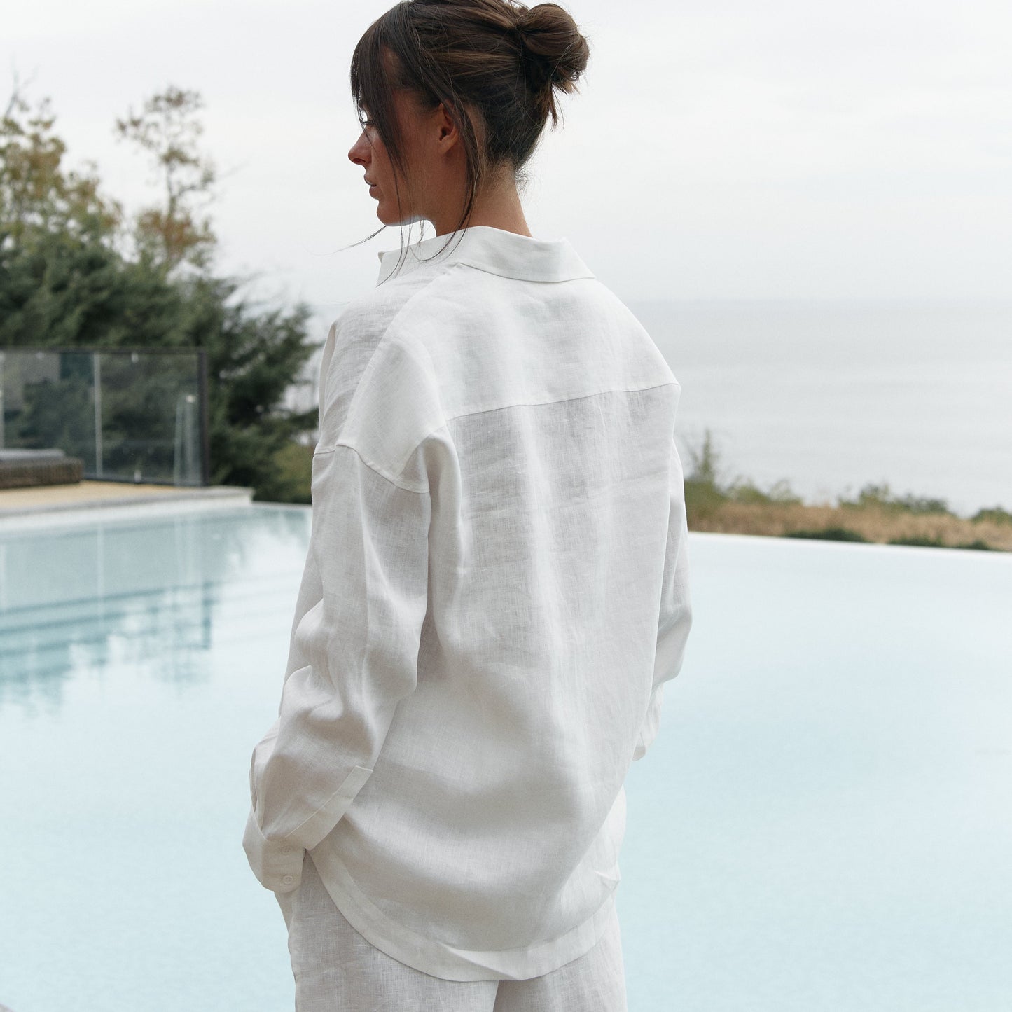 Woman in a white linen set, Nokaya, standing by a pool with a neutral background