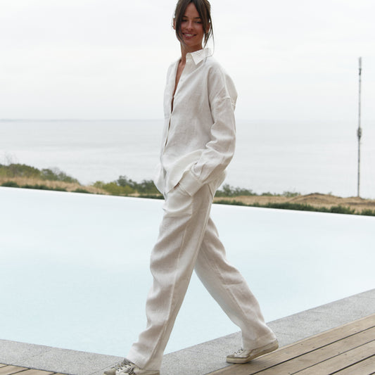  White linen pants and shirt on a woman standing on a wooden deck by a body of water.