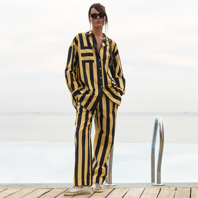 A woman wearing a black and yellow striped cotton shirt and pants, standing on a wooden deck with a white background
