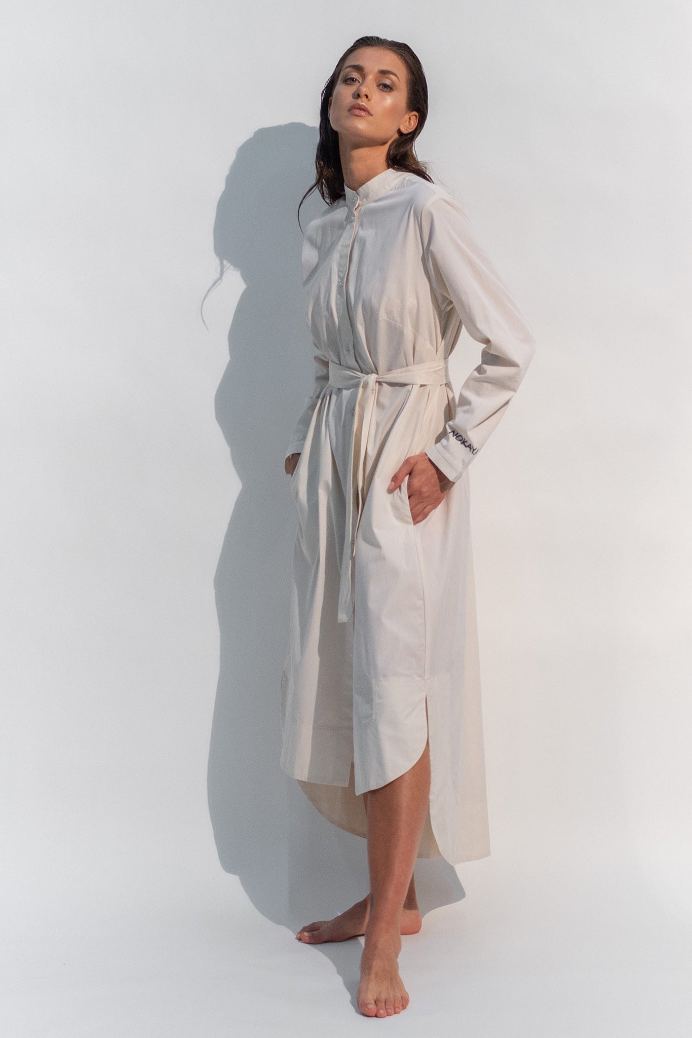 The Inner Matters cotton dress features a stylish, asymmetrical cut with a thin belt accentuating a silhouette.